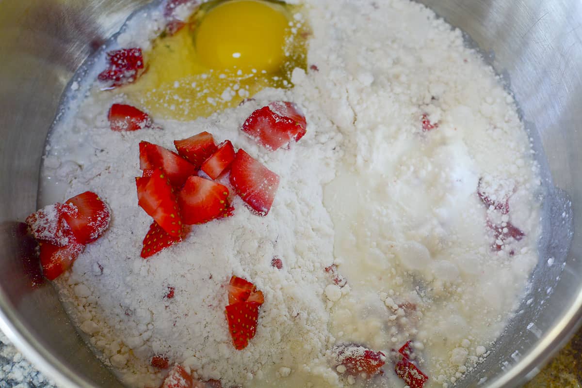 The muffin mix, egg and strawberry milk in a silver bowl. There are fresh strawberries in there as well.
