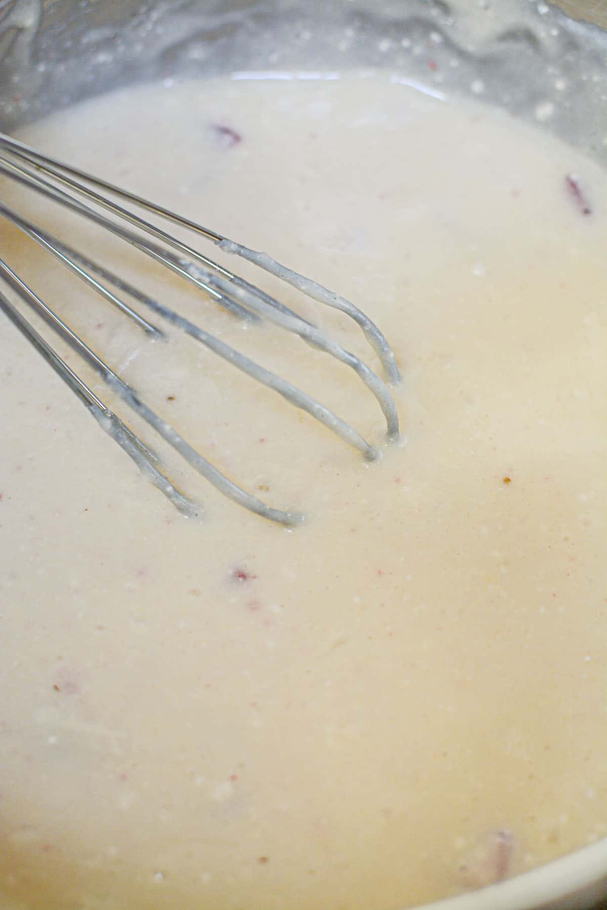 The strawberry pancake batter in a silver bowl, mixed, with a silver whisk sitting in the batter.