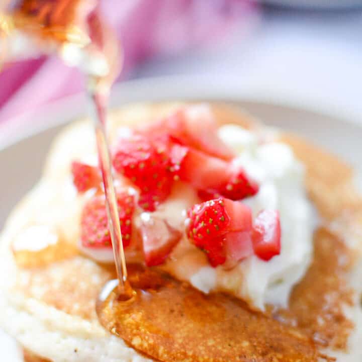 Syrup being poured over top stacked strawberry pancakes.
