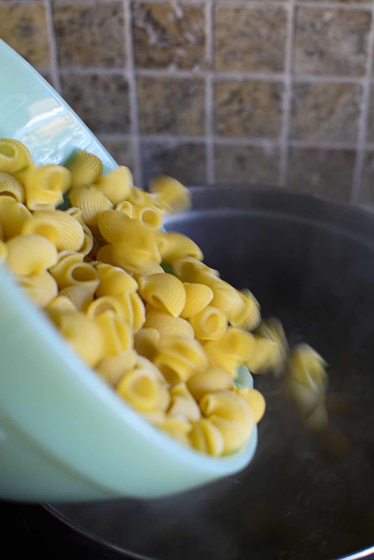 Adding the pasta that's in a green bowl to the boiling water. 