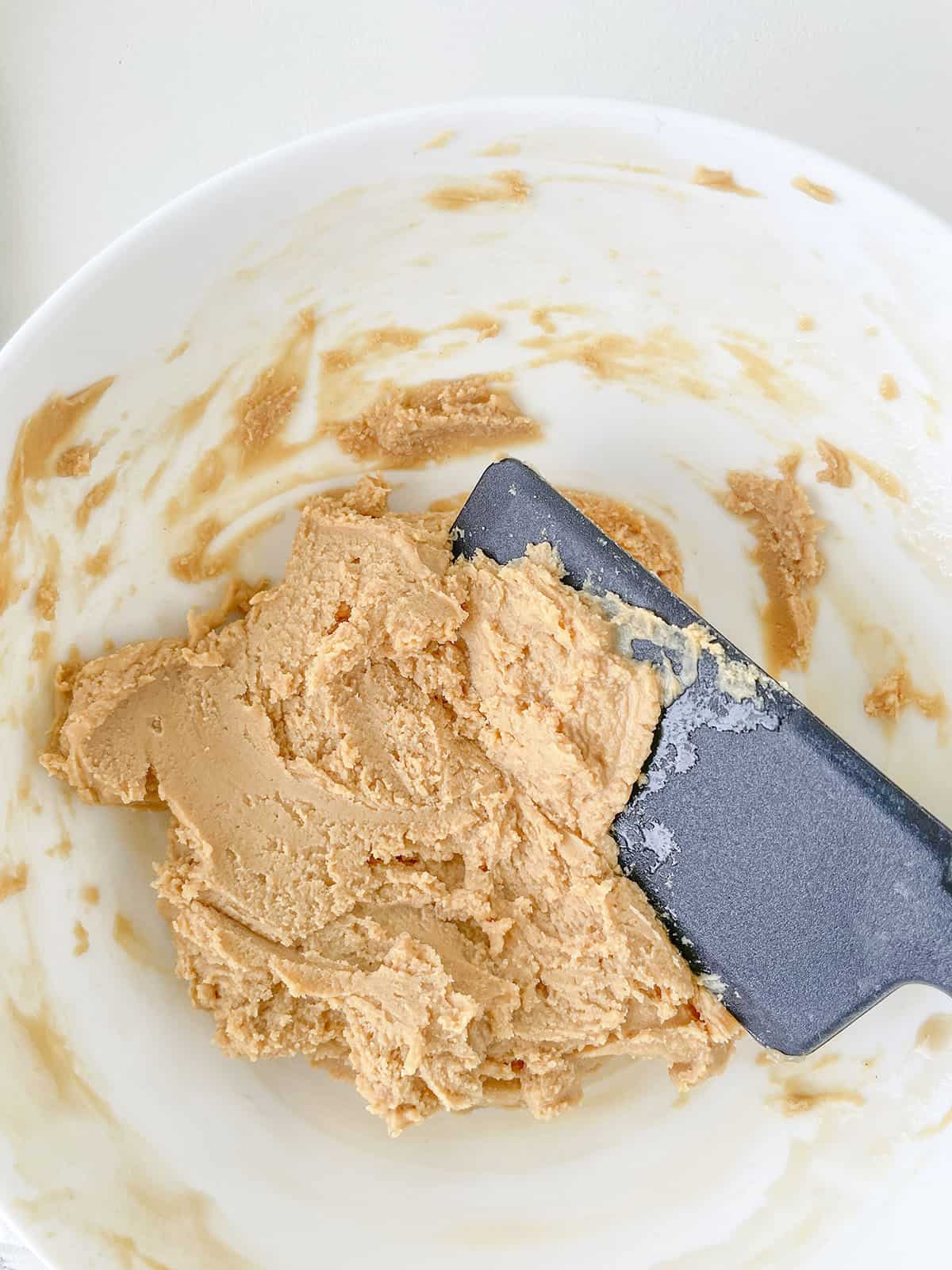 Mixing the cookie batter in a white bowl with a black spatula.