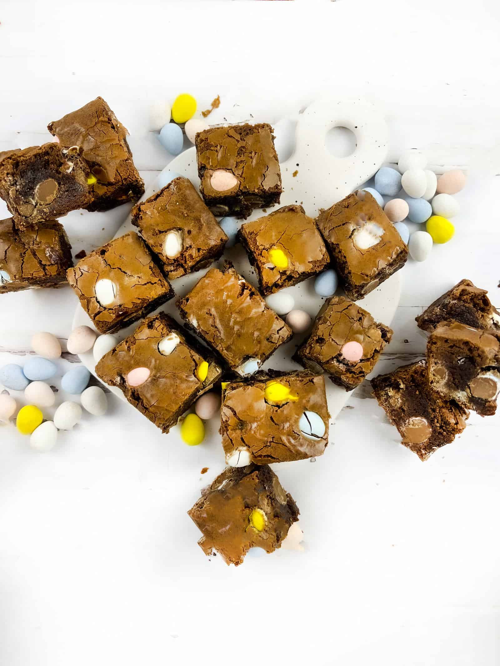 Easter brownies on a ceramic cutting board with mini eggs sprinkled around it.