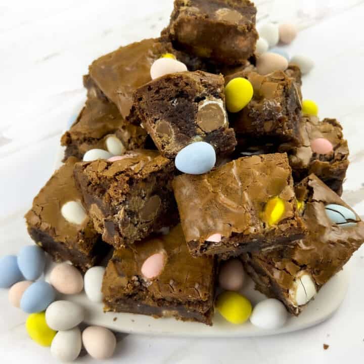 Brownies with easter eggs sprinkled around them on a white plate.