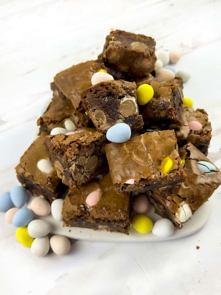 Brownies with easter eggs sprinkled around them on a white plate.