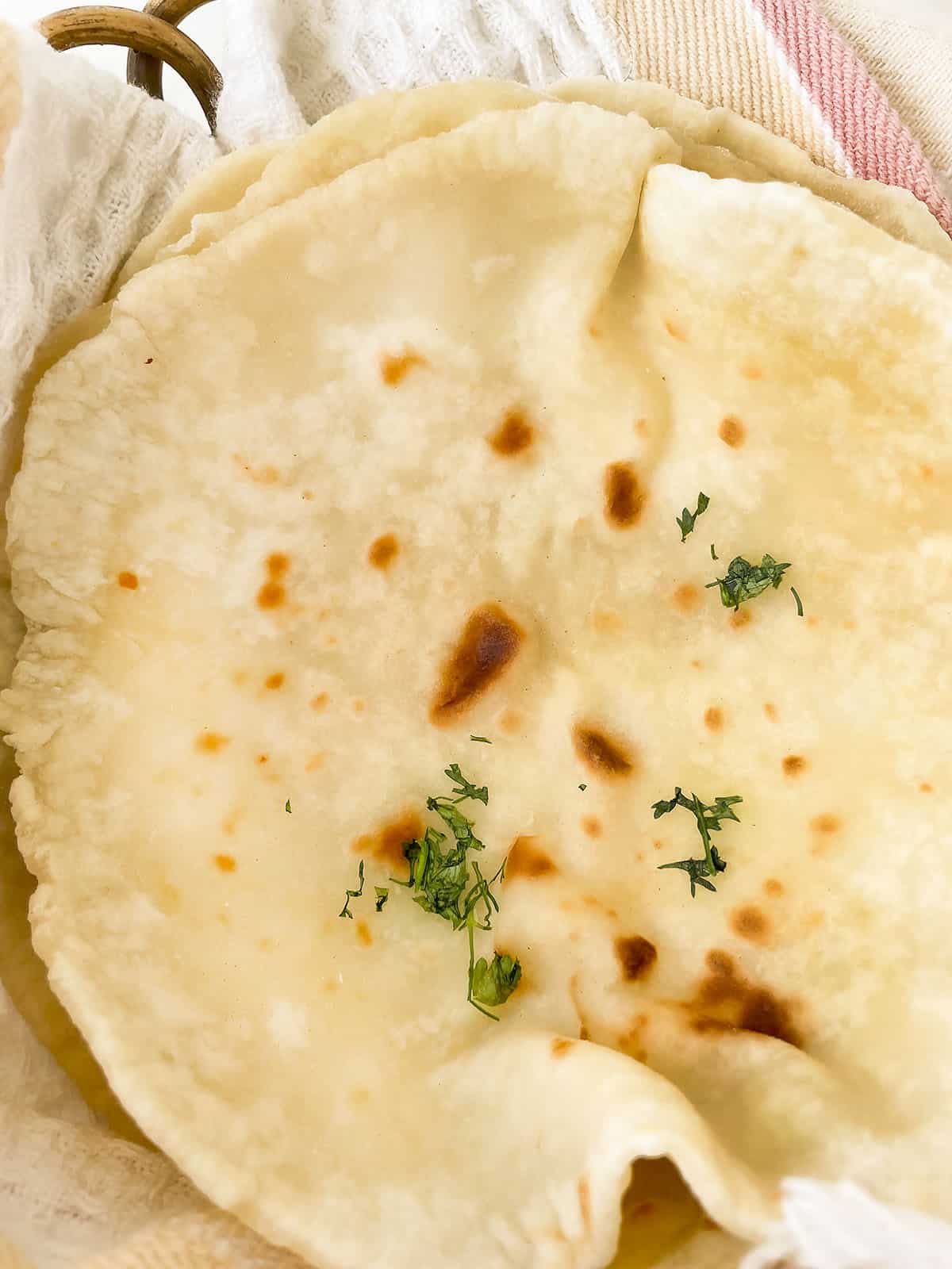 The naan breads sitting in a basket lined with a kitchen towel to keep soft.