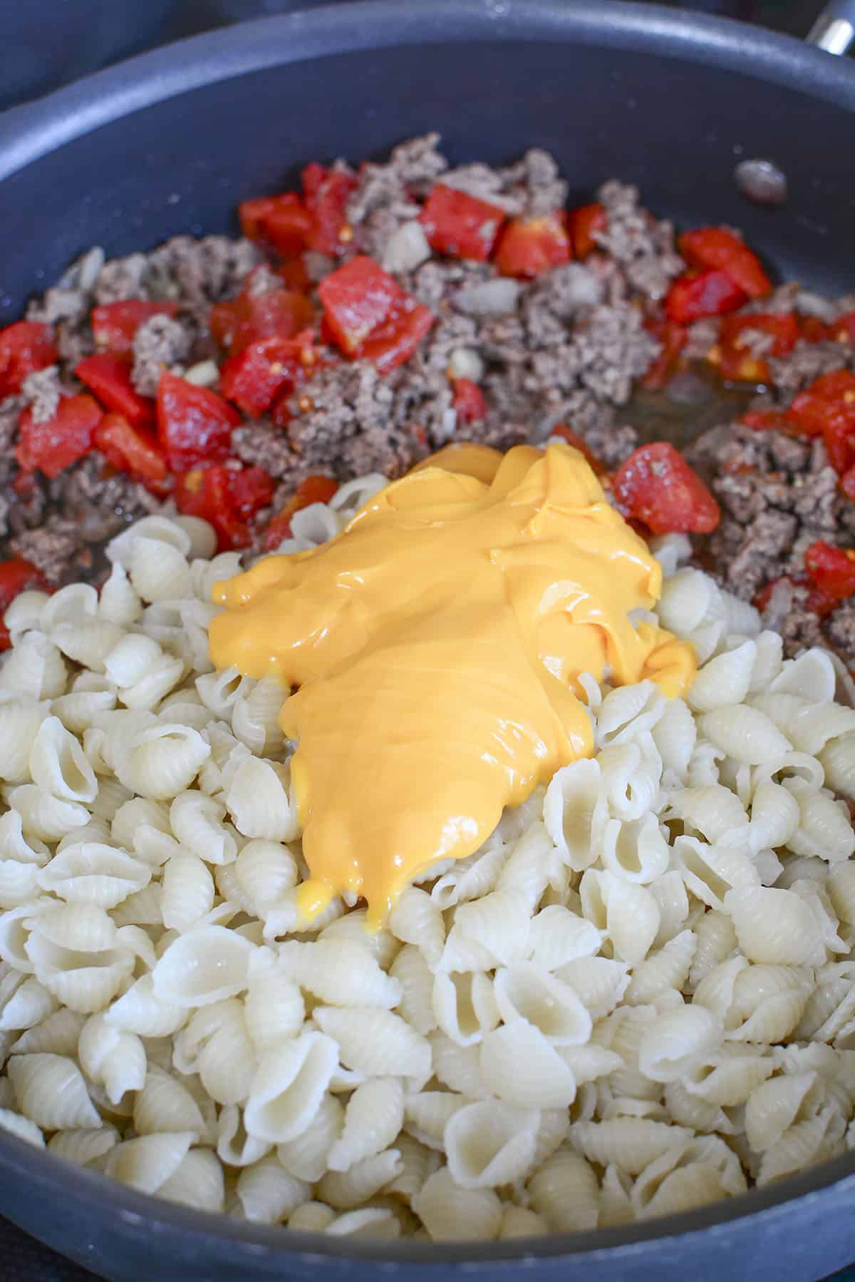 Ground beef cooked with tomatoes, pasta and cheese added to the pan.
