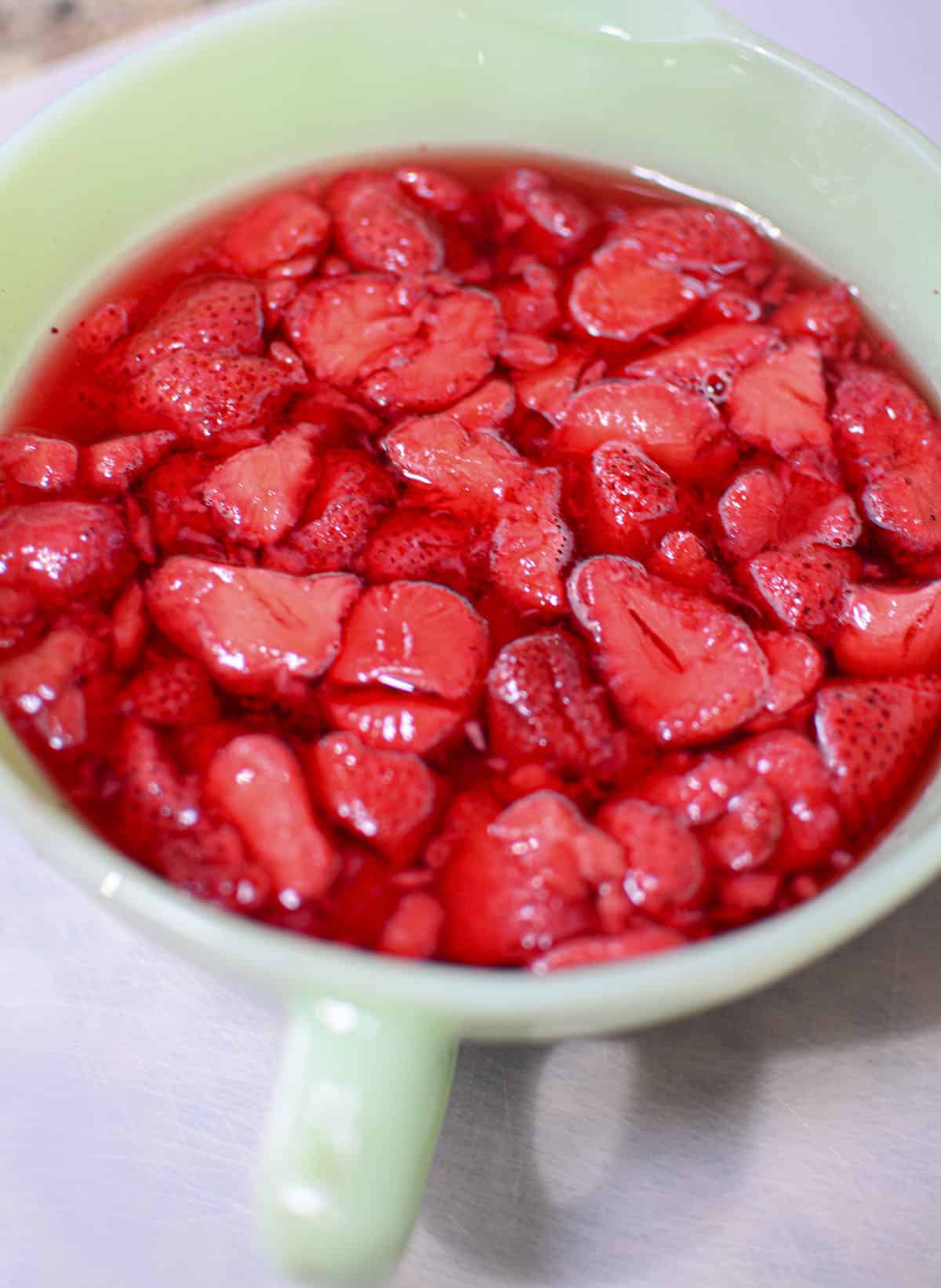 Strawberries added to jello in a green bowl.