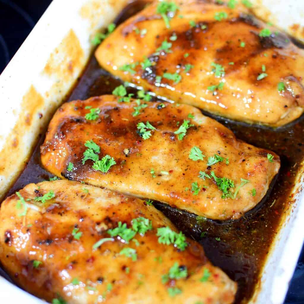 3 chicken breasts cooked in a white baking dish with sauce.