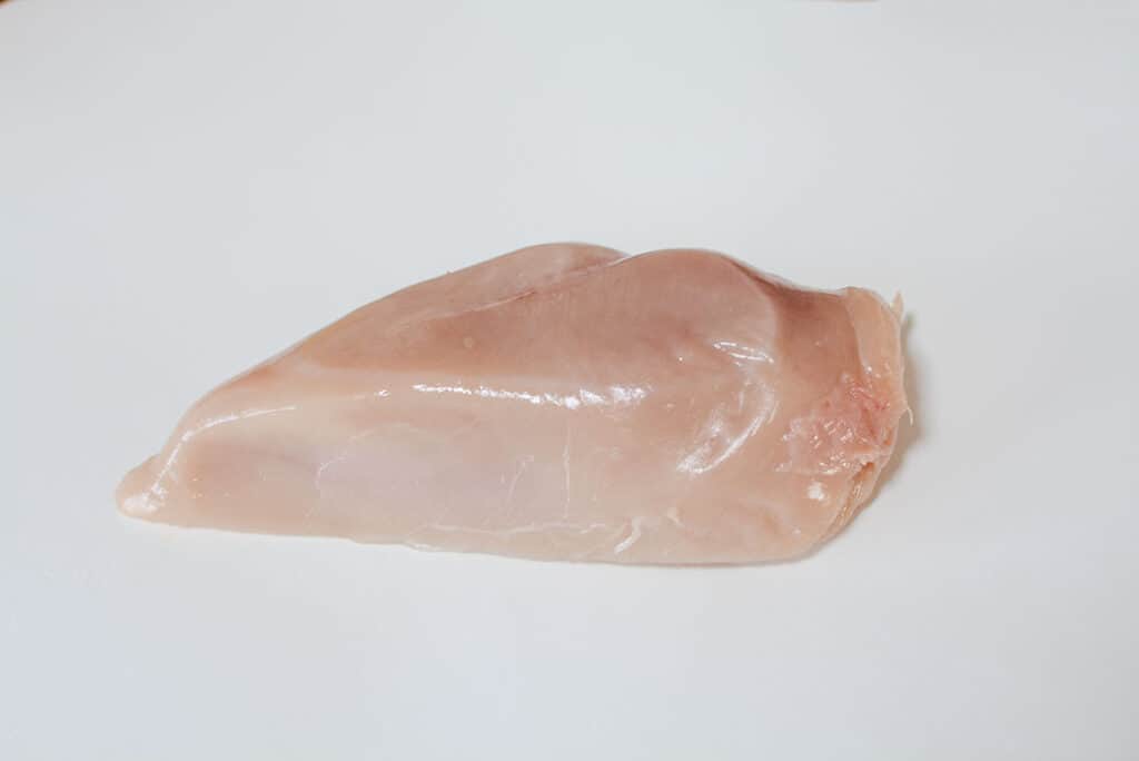 A chicken breast sitting on a white cutting board.