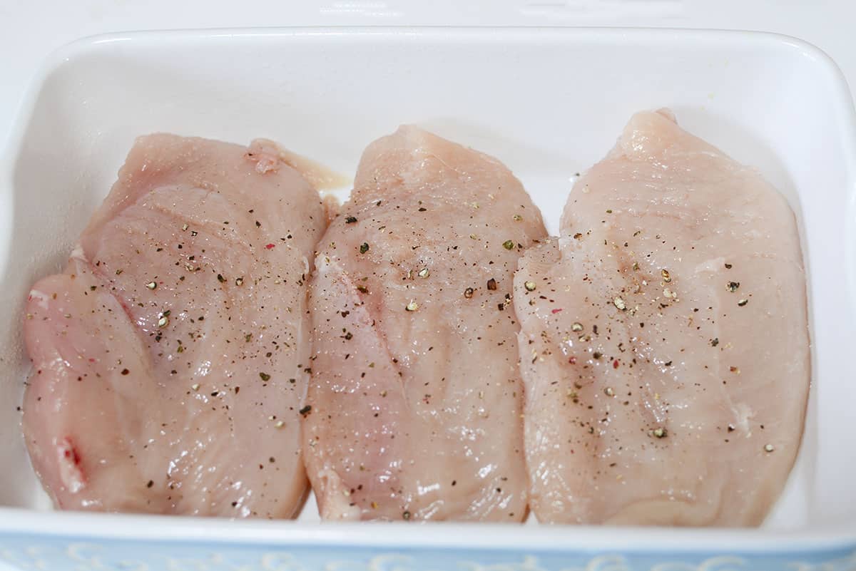 Raw chicken breasts seasoned with salt and pepper sitting n a blue and white baking dish.