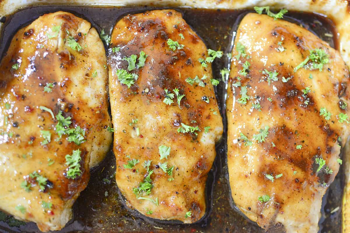 Three chicken breasts in a roasting pan with the brown sugar sauce over top and at the bottom of the dish. 