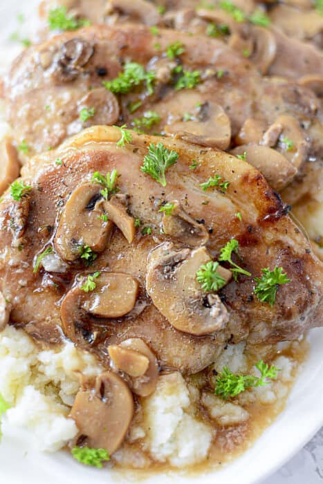 Pork chops and mushrooms in gravy on a white plate.