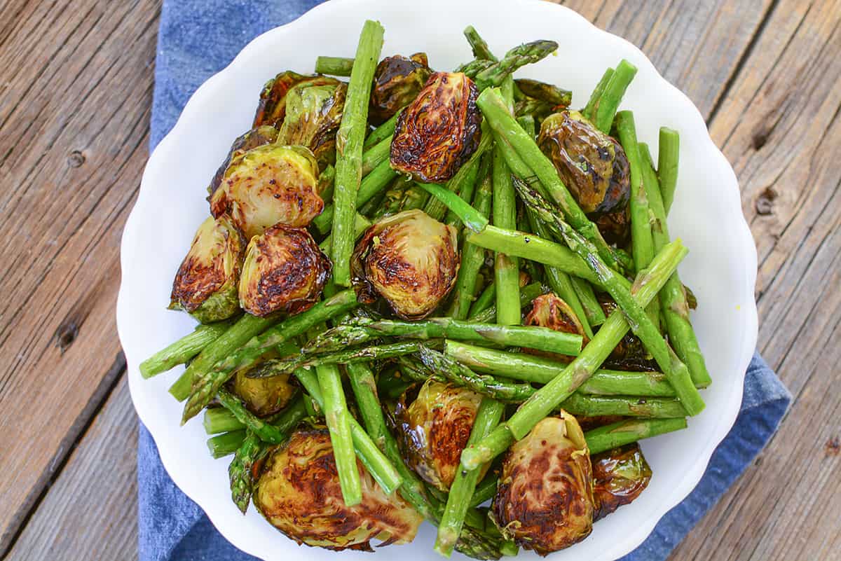 A roasted side dish of green veggies on a white plate on a wooden background.