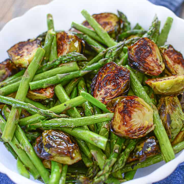 Roasted asparagus and brussels sprouts in a white bowl.