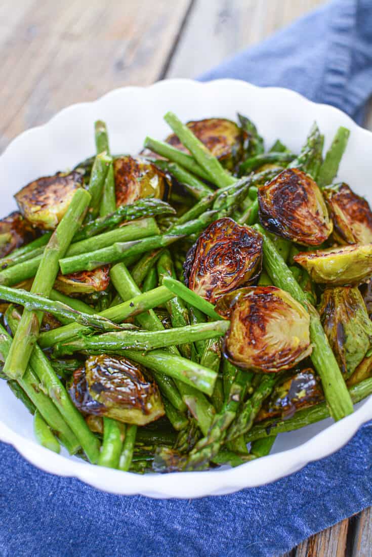 Roasted asparagus and brussels sprouts in a white bowl.