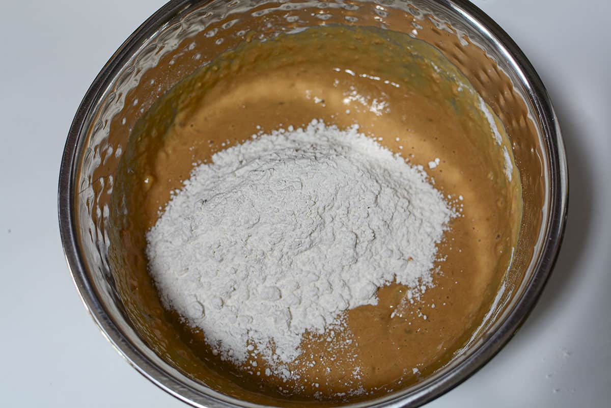 Mixing the flour into the batter in a silver bowl.