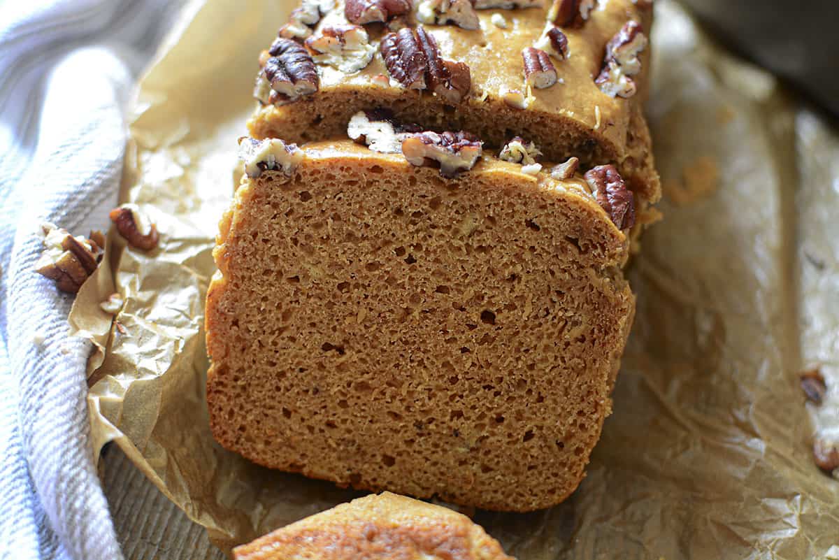 A slice of banana bread on parchment paper and pecans around it.