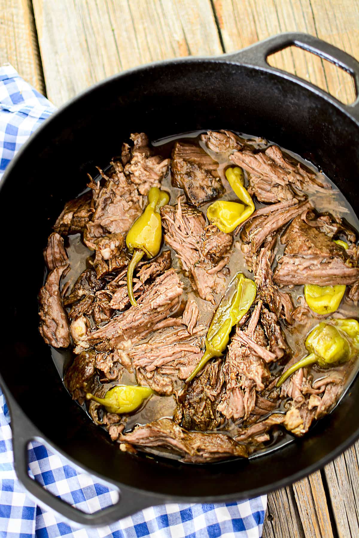 A chuck roast in a black dutch oven with peppers.