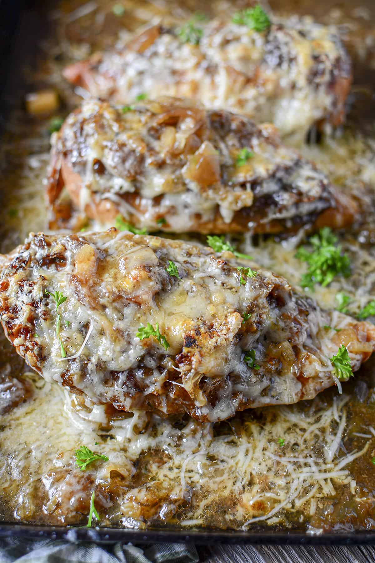 4 Ingredient Crock Pot French Onion Chicken topped with cheese in a cast iron pan.
