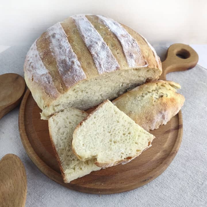 3 Ingredient artisan bread, sliced, sitting on a wooden cutting board.