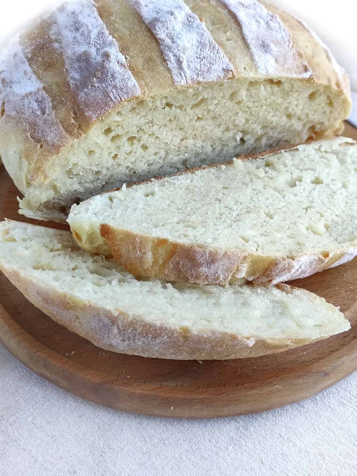 The bread loaf with two slices in the front, on a wooden cutting board.