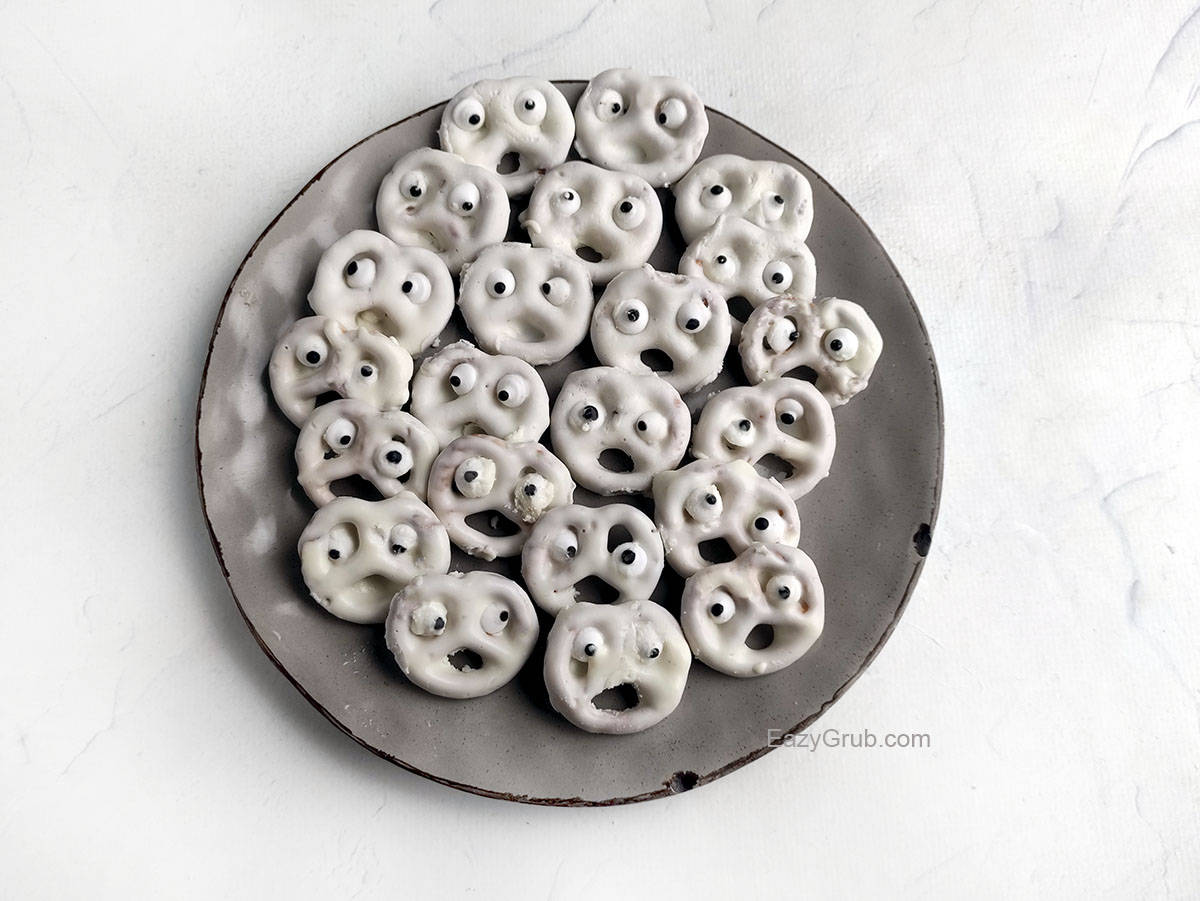 Lots of white chocolate dipped pretzels with candy eyes on a grey plate.