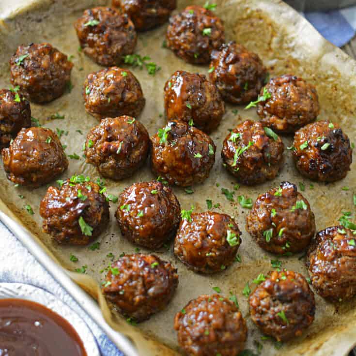 A square image of 4 ingredient oven baked BBQ meatballs on a baking sheet, garnished with parsley.