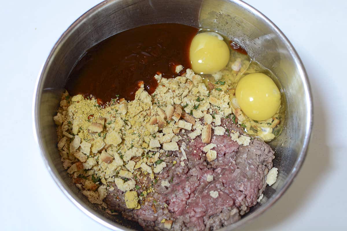 Four ingredients in a bowl. Ground beef, stuffing, eggs and bbq sauce.