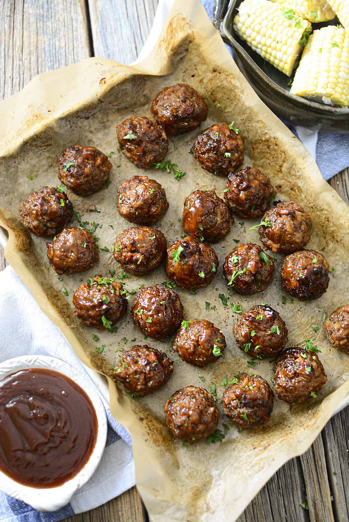 Meatballs on a baking sheet with corn on the upper right and bbq sauce on the bottom left.
