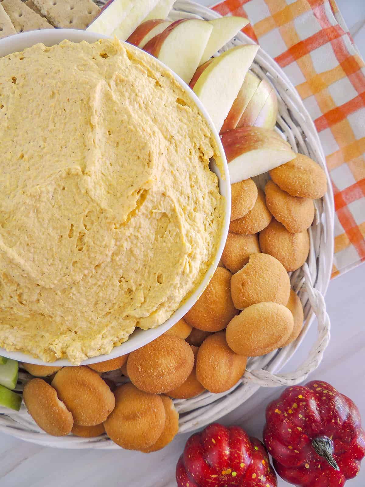 The pumpkin dip on the left with apple slices and nilla cookies on a basket underneath the dip. 