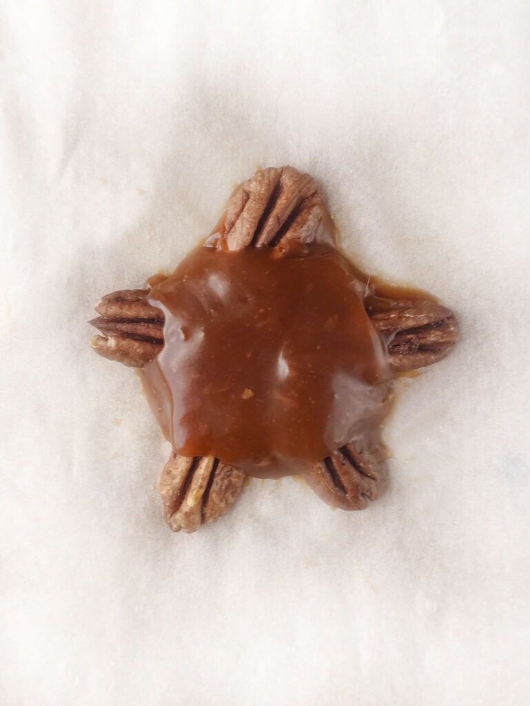 The caramel being placed on the pecans to form the body of the turtle treat.