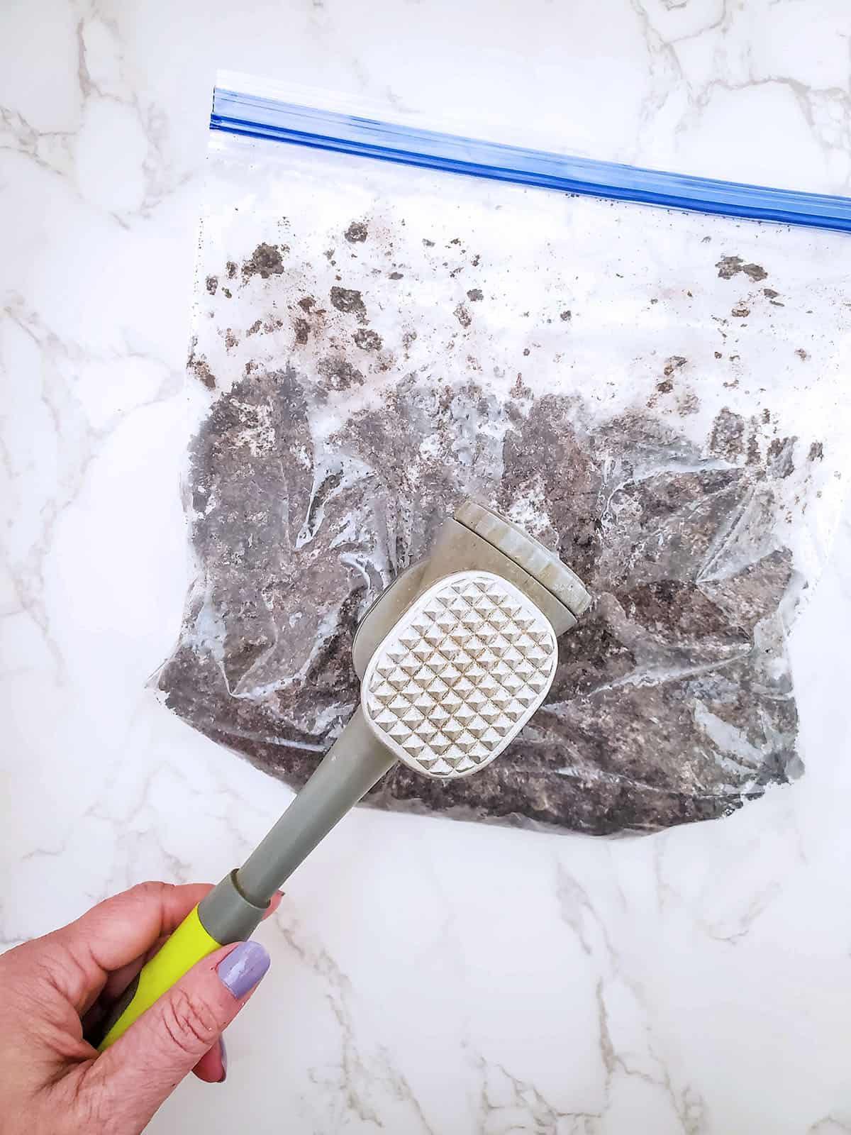The oreo crumbles being crushed with a kitchen mallet.