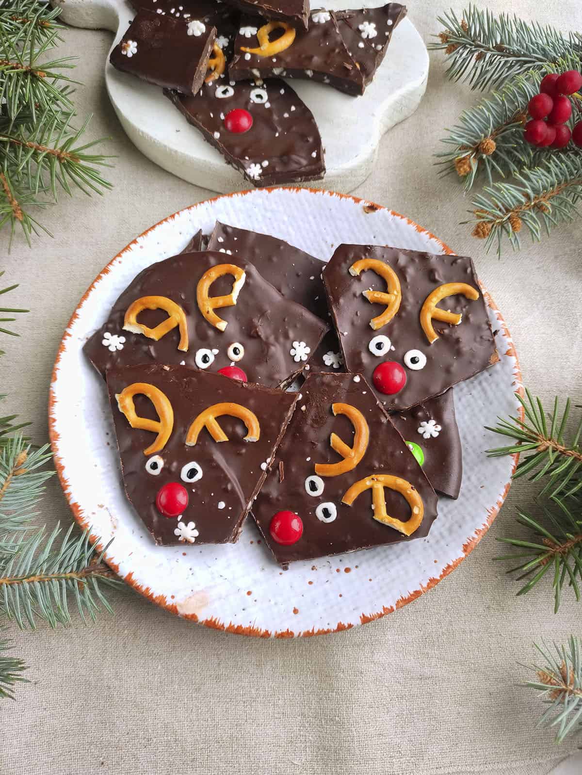 Pieces of chocolate almond bark on a white plate with christmas greenery around the plate.
