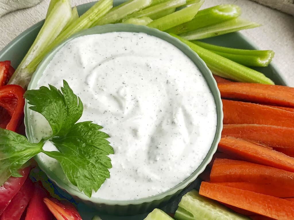 A large peice of parsley in on the bottom left of a bowl mixed with ranch dip.