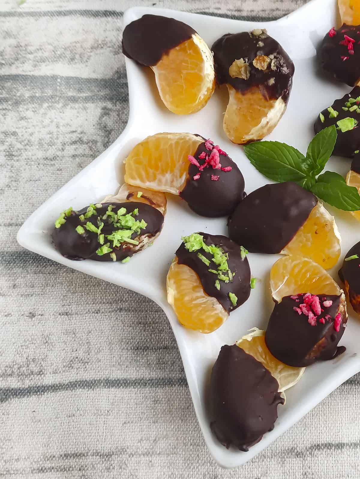 Chocolate covered orange slices on a white plate with different colored coconut on top.
