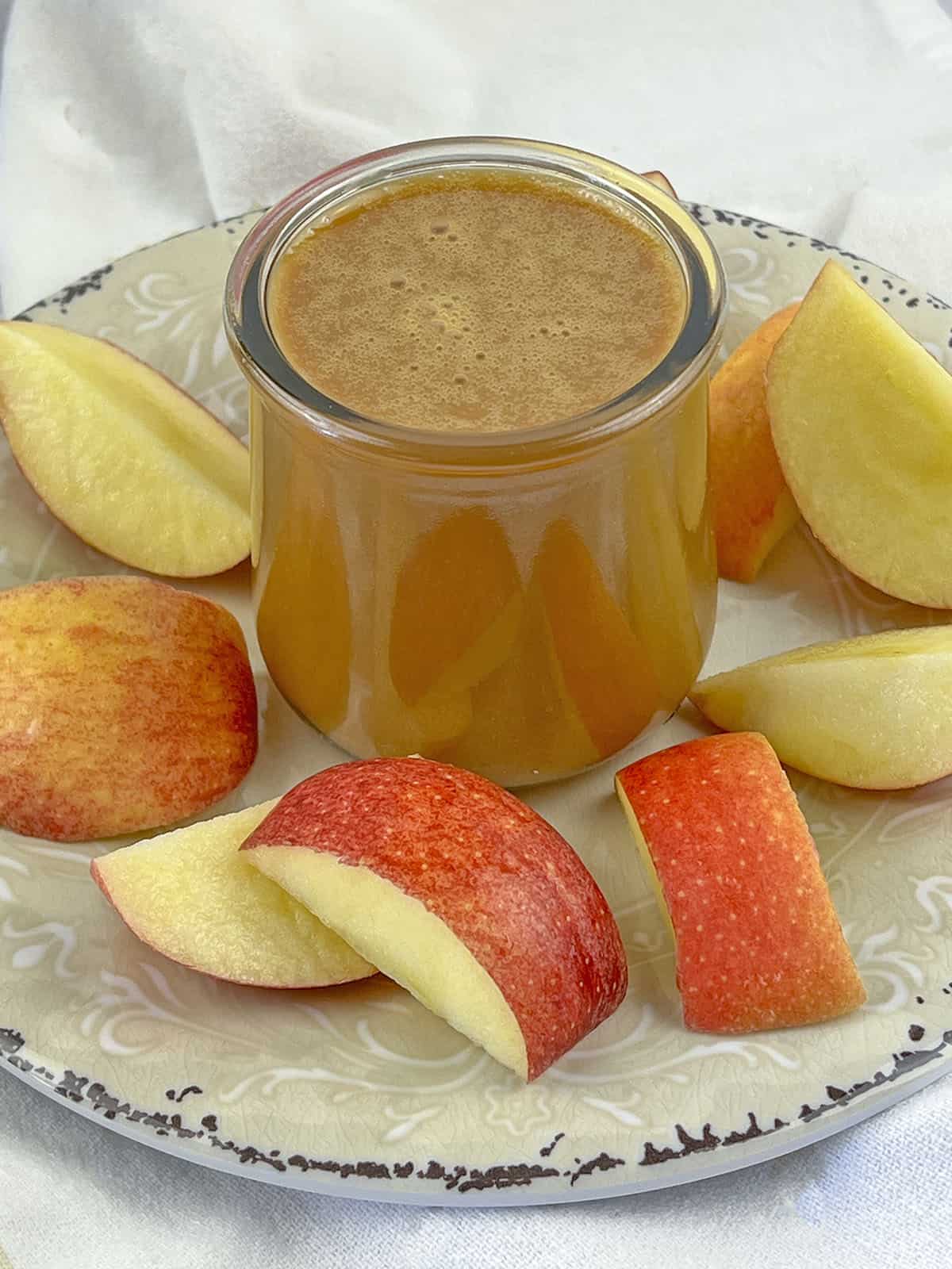 Caramel sauce in a glass jar with cut fruit around it.