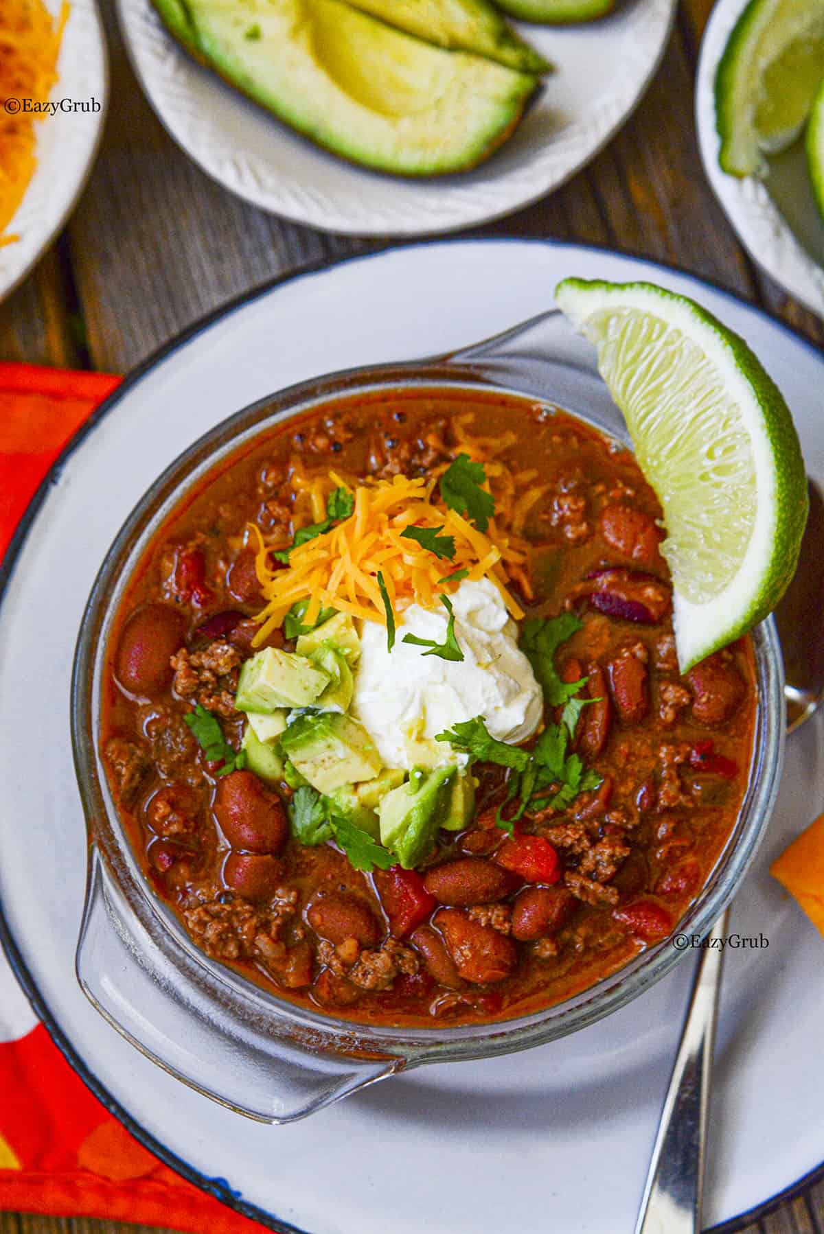 3 ingredient chili in a glass bowl on a white plate. A wedge of lime sits on the upper right corner of the bowl. Garnishes are in the center of the chili.