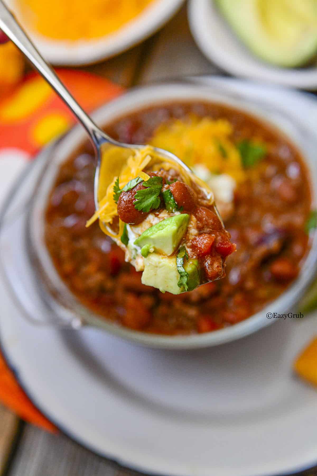 A spoonful of chili above a bowl of chili. 