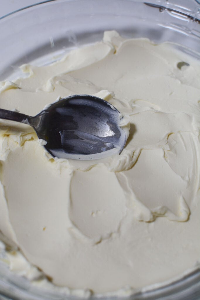 A spoon spreading out the cream cheese in the glass pie dish.