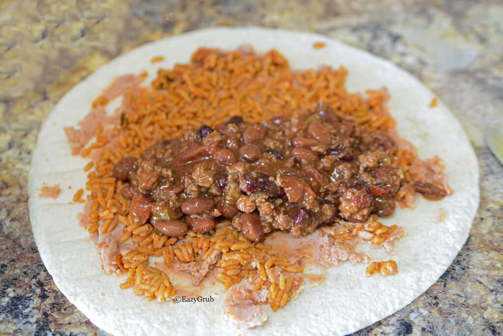 Seasoned rice and chili spread on top of the refried beans on a tortilla.
