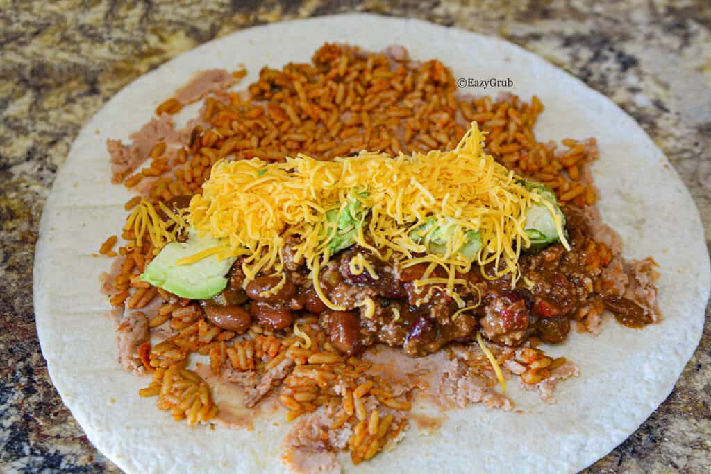 On top of the earlier ingredients, shredded cheese and diced avocado lay on top of the chili.