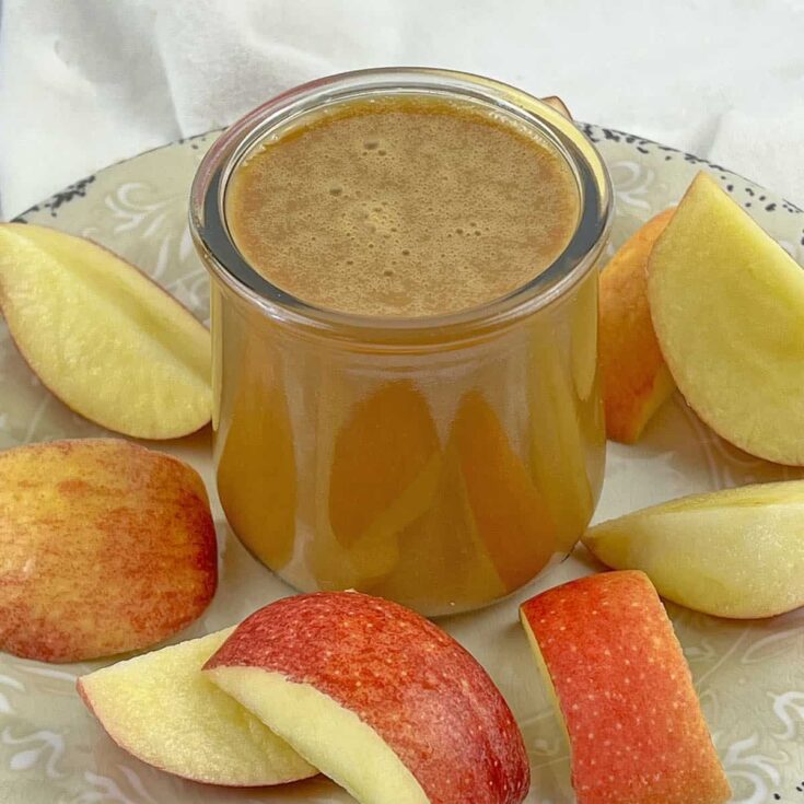 A jar of caramel sauce with cut apples on the plate around it.