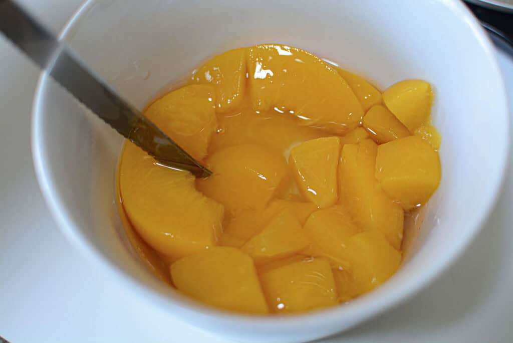 Cutting the peaches into smaller chunks because they are full slices in the container. 