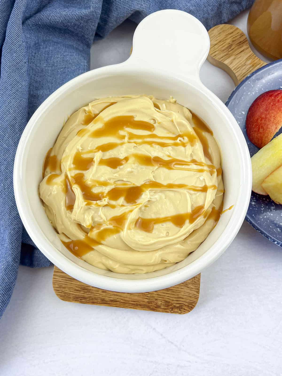 Caramel dip with extra caramel drizzled on top, in a white serving bowl. 