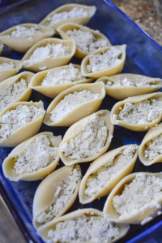The cheese mixture stuffed inside giant pasta shells in a blue casserole dish.