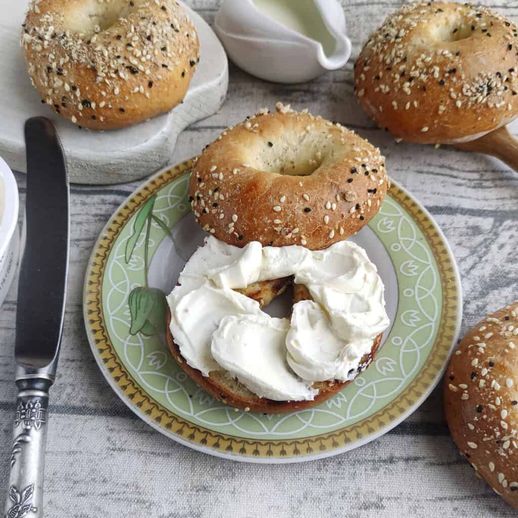 3 ingredient bagel square photo. One bagel cut in half on a plate, spread with cream cheese.
