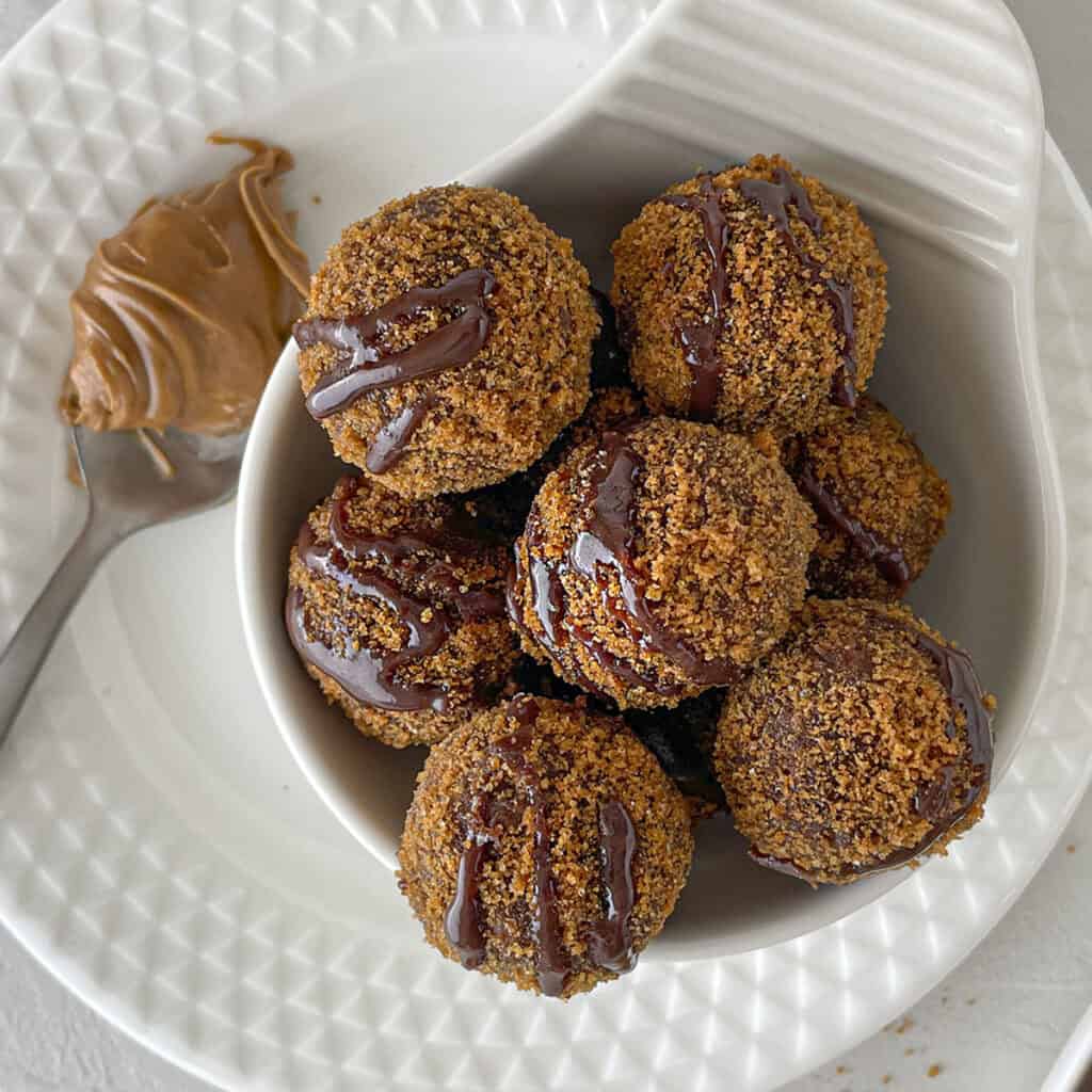 7 biscoff truffles in a white bowl with a spoonfull of biscoff spread on the upper left.