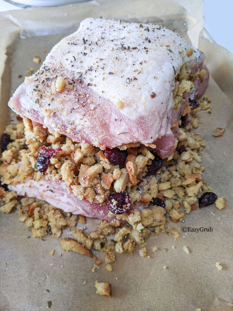 A stuffed pork loin roast with stuffing and cranberries on parchment paper.