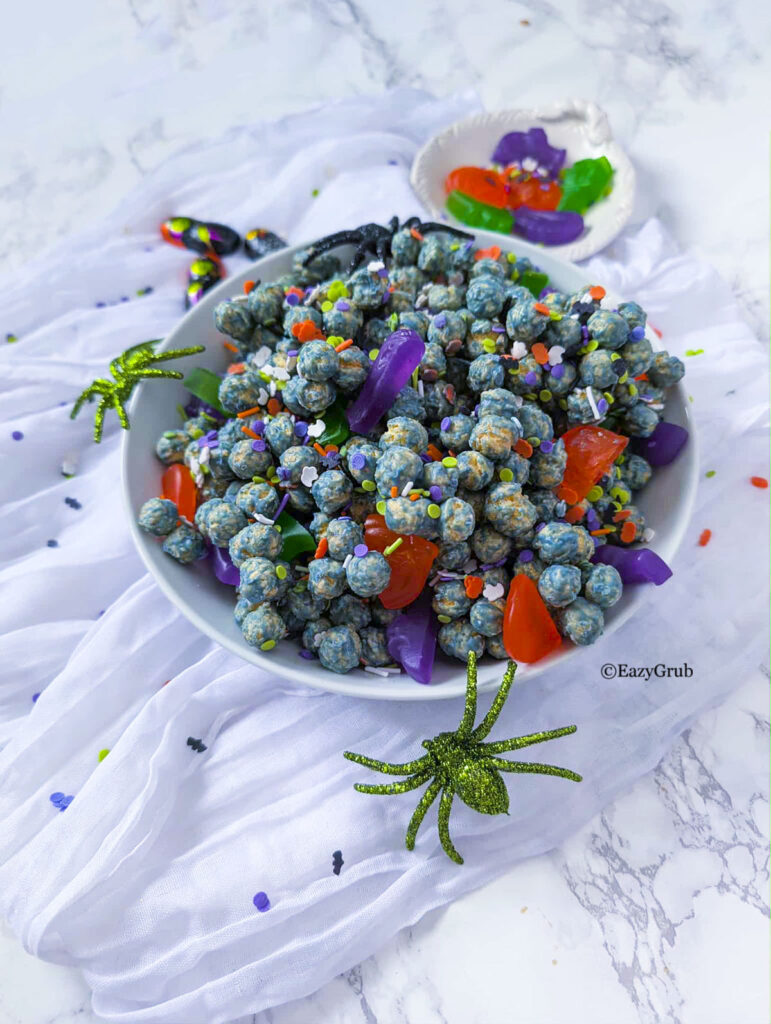Halloween candy treats in a white bowl with fake spiders around it.