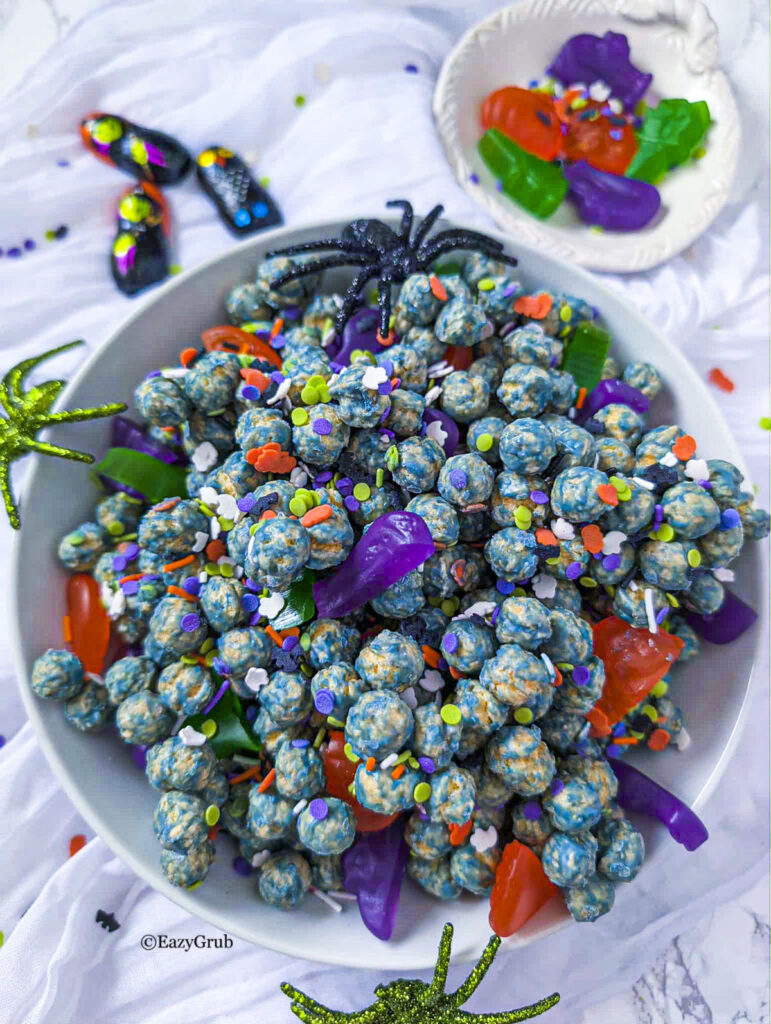 Frankenstien farts candy in a white bowl with candy and sprinkles on the table around the bowl.
